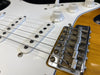 Close-up of electric guitar bridge, pickups, and control knobs on sunburst body with white pickguard, showing detailed strings and volume tone controls