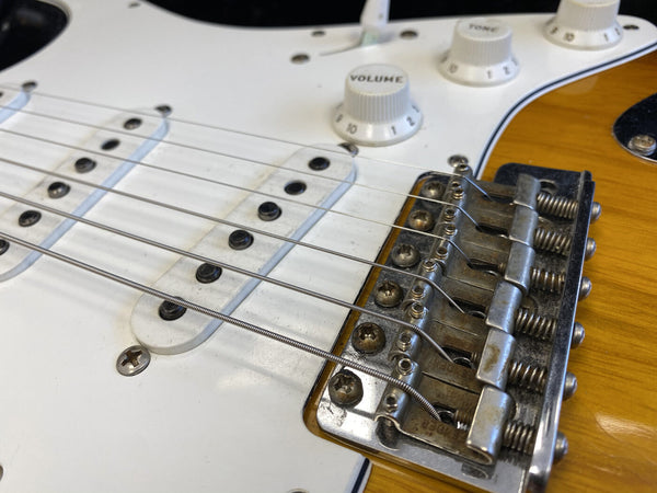 Close-up of electric guitar bridge, pickups, and control knobs on sunburst body with white pickguard, showing detailed strings and volume tone controls