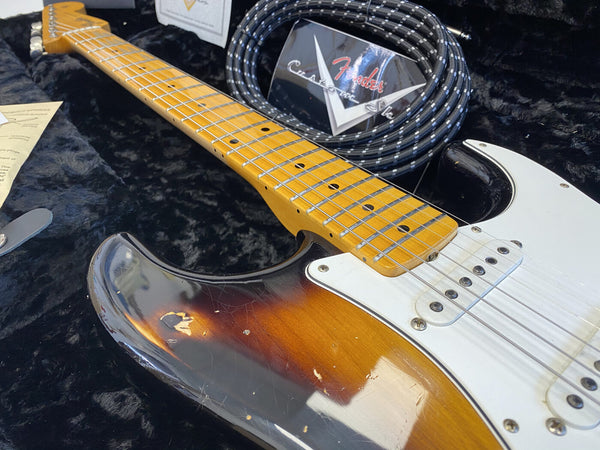 Close-up of vintage sunburst Fender Stratocaster electric guitar with maple neck and white pickguard inside black plush guitar case with coiled Fender Custom Shop instrument cable