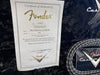 Fender Custom Shop Certificate of Authenticity for Post Mod Strat JM Relic guitar dated 02/13/17 with serial number 1413 on black plush guitar case lining next to coiled black and white Fender instrument cable and Fender Custom Shop logo tag.