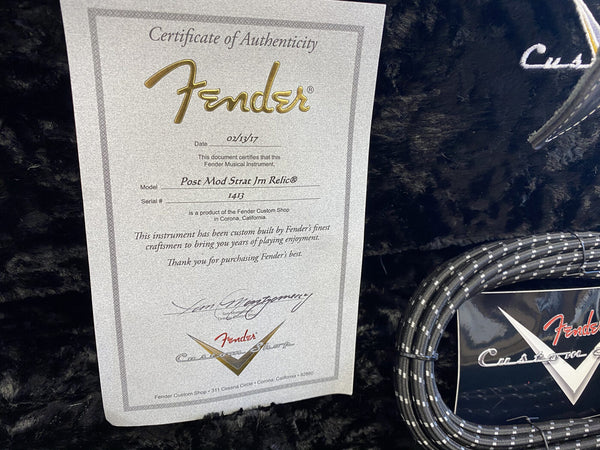 Fender Custom Shop Certificate of Authenticity for Post Mod Strat JM Relic guitar dated 02/13/17 with serial number 1413 on black plush guitar case lining next to coiled black and white Fender instrument cable and Fender Custom Shop logo tag.
