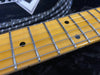 Close-up of maple guitar fretboard with chrome frets and black dot inlays on electric guitar strings