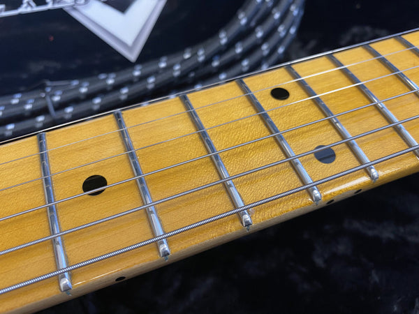 Close-up of maple guitar fretboard with chrome frets and black dot inlays on electric guitar strings