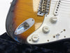Close-up of vintage sunburst electric guitar body showing input jack, volume and tone control knobs, and white pickguard on black plush background