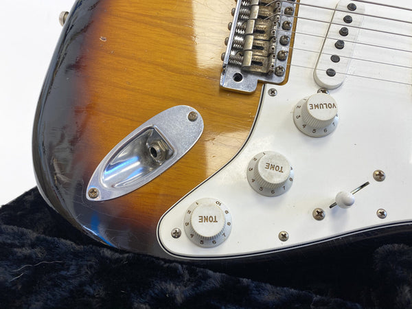 Close-up of vintage sunburst electric guitar body showing input jack, volume and tone control knobs, and white pickguard on black plush background
