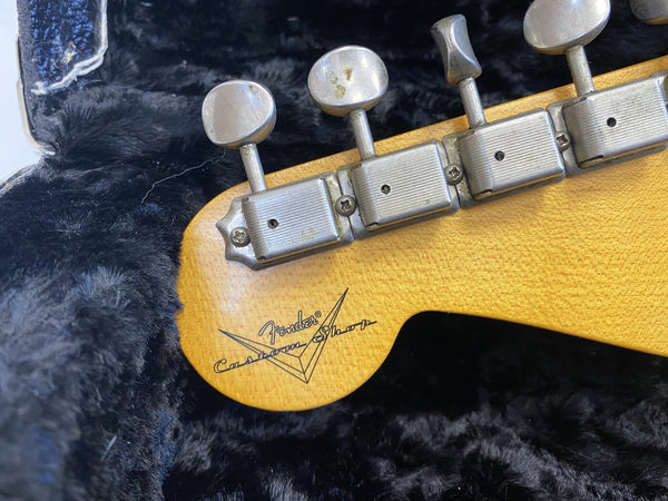 Close-up of vintage Fender Custom Shop guitar headstock with tuning pegs and logo on maple wood, resting on black plush guitar case lining