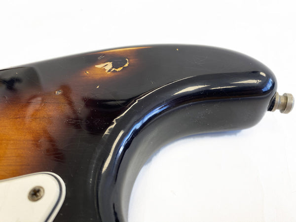 Close-up of a sunburst electric guitar body showing wear and paint chips on the upper horn and black finish with visible scratches and aging.