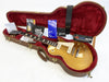 Gibson Les Paul Standard Gold Top electric guitar in brown hard case with red plush interior, included warranty, owner's manual, and black Gibson leather strap.