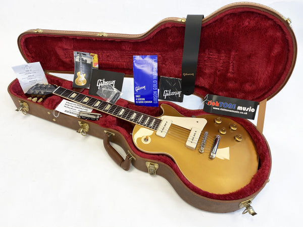 Gibson Les Paul Standard Gold Top electric guitar in brown hard case with red plush interior, included warranty, owner's manual, and black Gibson leather strap.