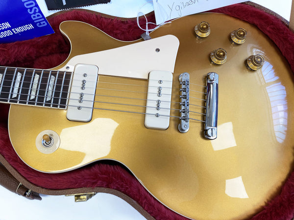 Close-up of gold electric guitar with white pickguard and two single-coil pickups inside red plush guitar case