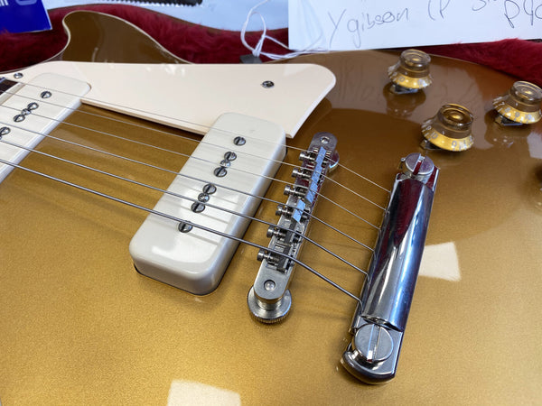 Close-up of gold electric guitar bridge, white P90 pickups, and gold control knobs on glossy finish guitar body at Coffee House Guitars