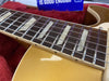 Close-up of electric guitar fretboard with pearl block inlays, metal frets, and silver strings on a gold finish body resting on a red plush background