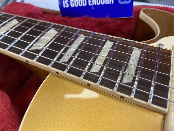 Close-up of electric guitar fretboard with pearl block inlays, metal frets, and silver strings on a gold finish body resting on a red plush background