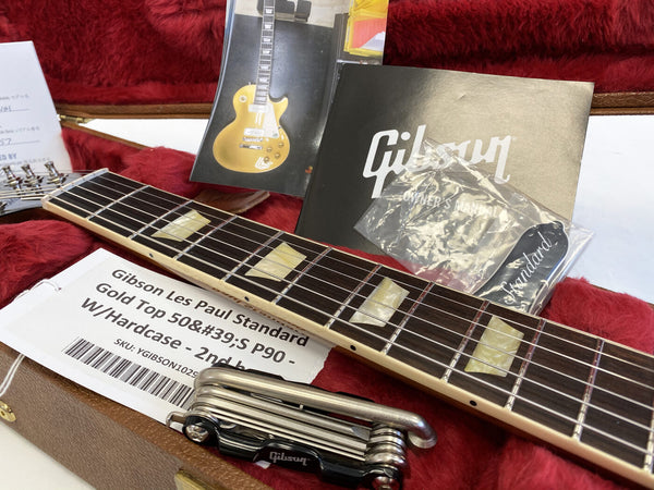 Close-up of Gibson Les Paul Standard Gold Top 50's P90 guitar neck and fretboard with owner’s manual, guitar maintenance tool, extra truss rod cover, and certificate inside red plush-lined hard case