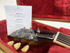 Close-up of Gibson Les Paul guitar headstock with tuning pegs and inspection certificate inside red plush-lined guitar case