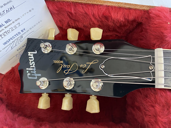 Close-up of Gibson Les Paul guitar headstock with vintage tuning pegs on red plush guitar case lining and inspection certificate in background
