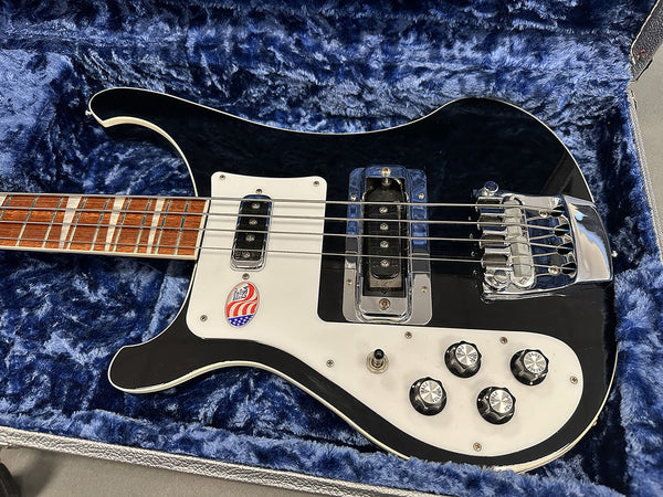 Black electric bass guitar with white pickguard, chrome bridge, and control knobs in a blue plush-lined guitar case