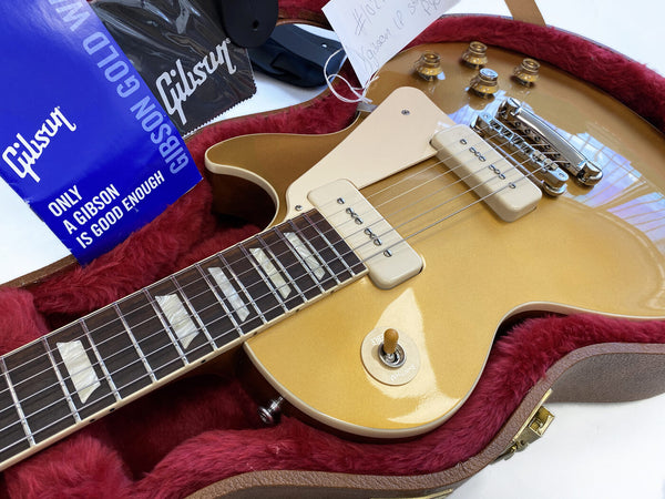 Close-up of Gibson electric guitar with gold top finish and P90 pickups in red plush-lined hard case with Gibson polishing cloth and accessories