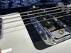 Close-up of electric guitar strings and chrome pickup cover on white guitar body with black pickguard background