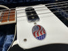 Close-up of electric guitar white pickguard with metal pickup and USA made sticker, showing part of wooden fretboard and strings in guitar case with blue plush lining.