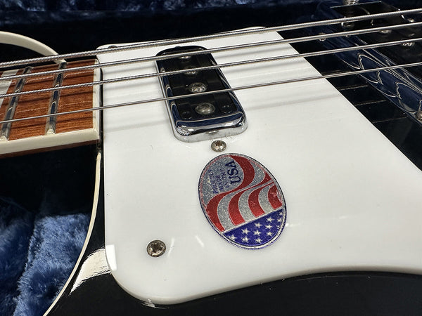Close-up of electric guitar white pickguard with metal pickup and USA made sticker, showing part of wooden fretboard and strings in guitar case with blue plush lining.