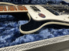 Close-up of black and white electric guitar body and fretboard resting on blue plush interior of guitar case