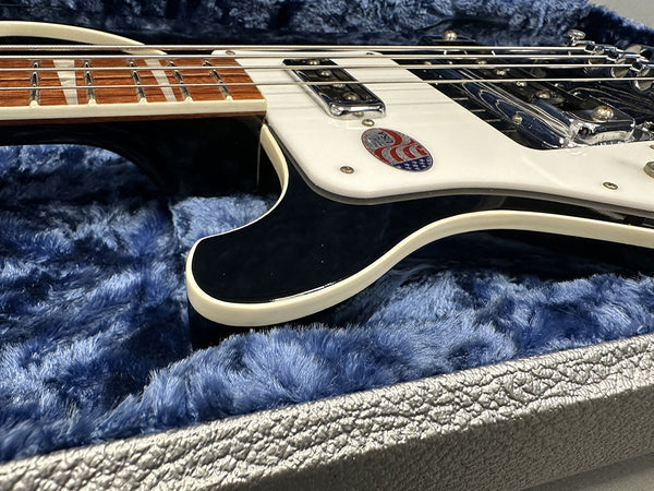 Close-up of black and white electric guitar body and fretboard resting on blue plush interior of guitar case