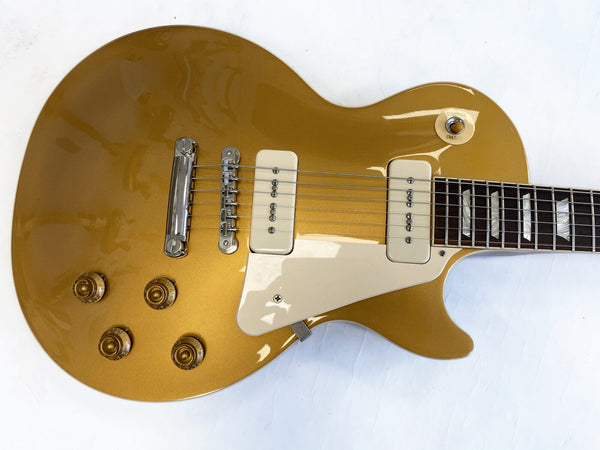 Gold electric guitar with cream-colored pickups and pickguard, four control knobs, and rosewood fretboard with rectangular inlays on white background