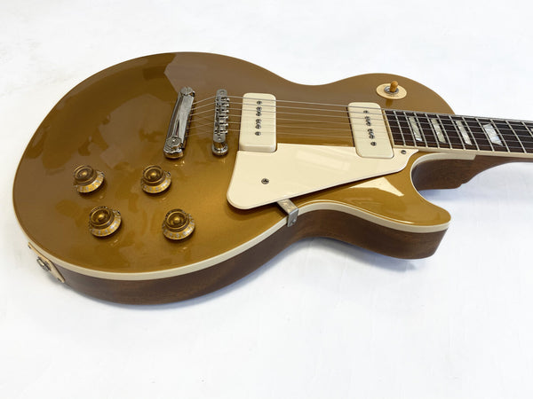 Goldtop electric guitar with cream pickguard and dual cream pickups on white background