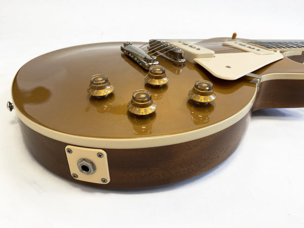 Close-up of gold top electric guitar body with cream binding, four amber control knobs, and chrome bridge and pickup covers on white background