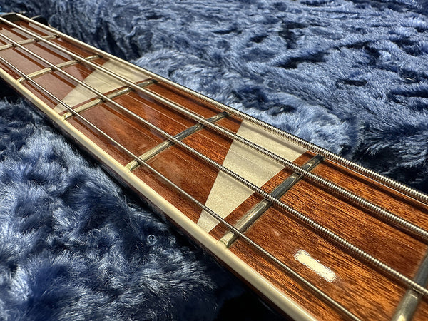 Close-up of bass guitar fretboard with metal frets and four strings on soft blue fabric background