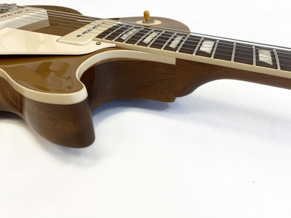 Close-up of gold and cream electric guitar body and neck joint with rosewood fretboard and trapezoid inlays on white background