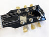 Close-up of black Gibson Les Paul electric guitar headstock with vintage tuners and white binding on white background