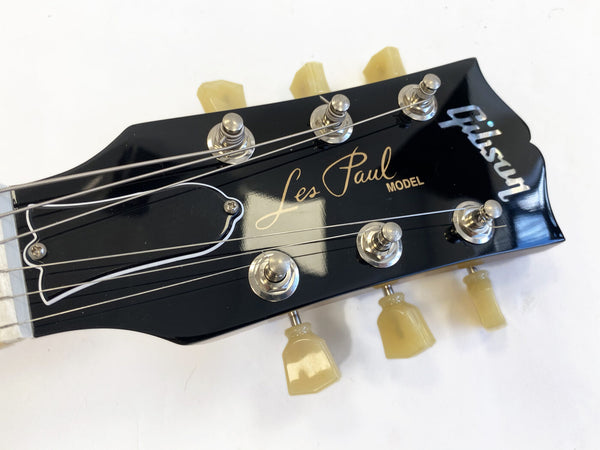 Close-up of black Gibson Les Paul electric guitar headstock with vintage tuners and white binding on white background