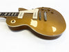 Close-up of gold electric guitar body with white pickguard, two cream single-coil pickups, four amber control knobs, and a wooden neck on white background
