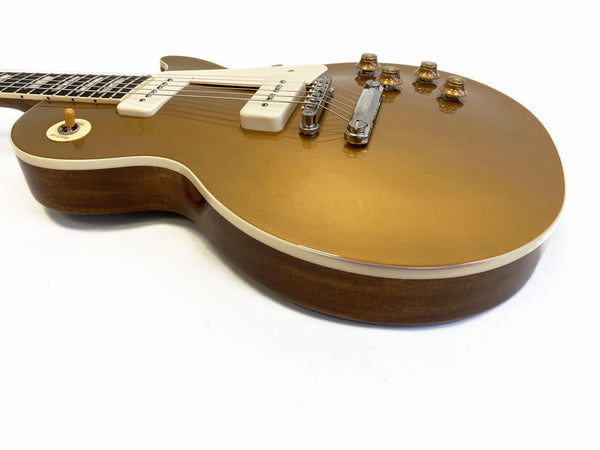 Gold top electric guitar with cream binding, white pickup covers, and amber control knobs on a brown wooden body, close-up angle on white background