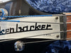 Close-up of Rickenbacker bass guitar headstock with strings and tuner knobs on blue textured background