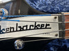 Close-up of Rickenbacker bass guitar headstock with strings and tuning pegs on blue plush case background