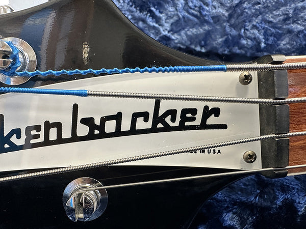 Close-up of Rickenbacker bass guitar headstock with strings and tuning pegs on blue plush case background