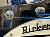 Close-up of black Rickenbacker guitar headstock with blue strings wound around tuning pegs and partial logo visible