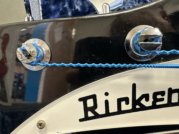 Close-up of black Rickenbacker guitar headstock with blue strings wound around tuning pegs and partial logo visible
