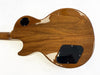 Back of solid wood electric guitar body with glossy finish and black control cavity covers against white background