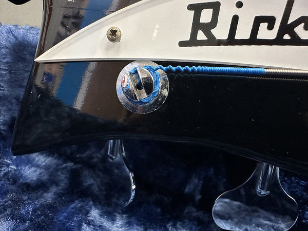 Close-up of a black electric bass guitar with blue-wrapped strings and chrome bridge detail on a soft blue fabric background.