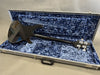 Black electric bass guitar lying face down inside open grey hard case with blue plush interior, showing back of guitar and tuning keys, Rickenbacker branded case