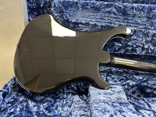 Black electric guitar body and neck showing glossy finish with light scratches, resting on blue plush guitar case interior