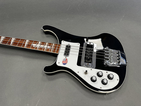Black and white electric bass guitar with rosewood fretboard and four control knobs on gray background