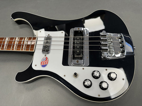 Black and white electric bass guitar with chrome bridge and pickups, four control knobs, and rosewood fretboard on gray background