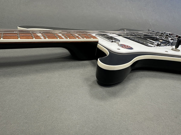 Close-up angled view of black electric guitar body and rosewood fretboard with white binding and chrome hardware on gray surface.