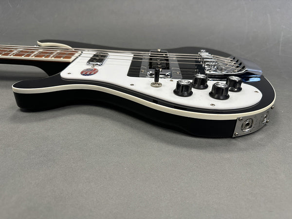 Black electric bass guitar with white pickguard and chrome hardware on gray background