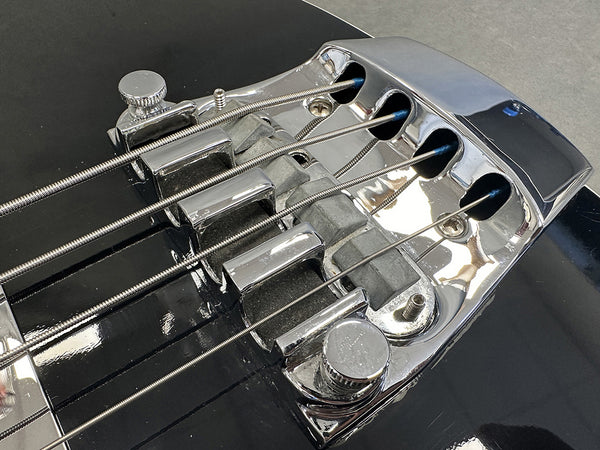 Close-up of chrome bridge and strings on black electric bass guitar showing detailed string saddles and adjustment knobs